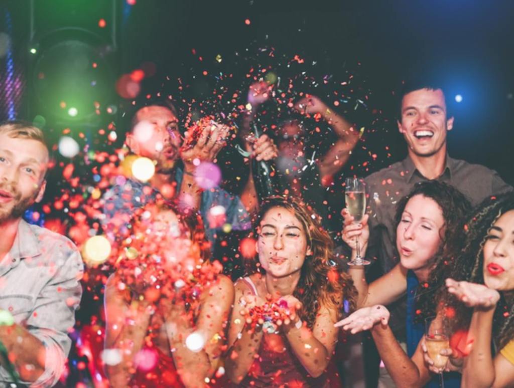 Happy friends doing party throwing confetti in nightclub - Group young people having fun celebrating new year holidays together in disco club, new year's eve concept.